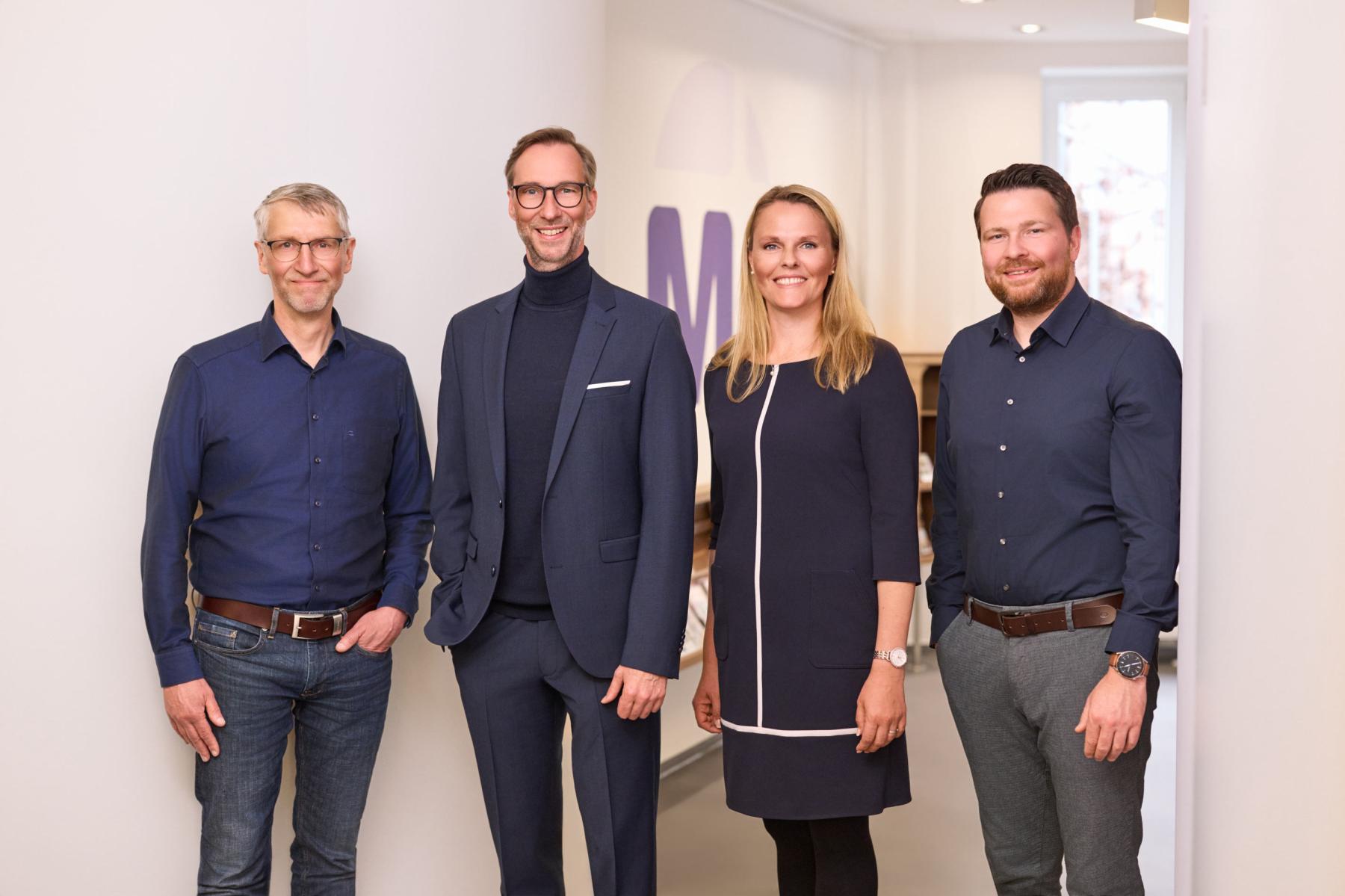 Portr?tcollage von vier l?chelnden Personen vor unterschiedlich farbigen Hintergr?nden, angeordnet in einem Raster.