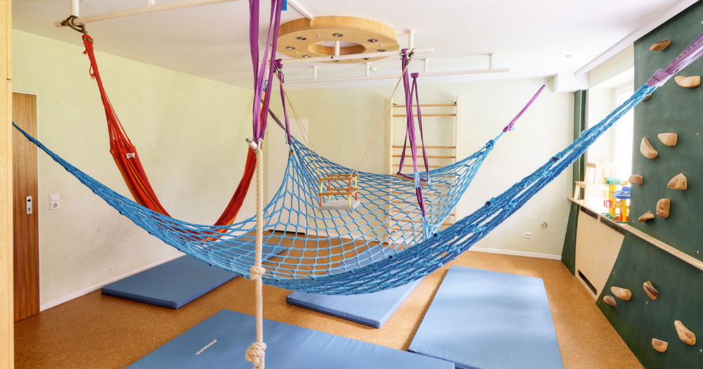 Spielzimmer f?r Kinder mit H?ngematten, Kletterm?glichkeiten und blauen Matten auf dem Boden.