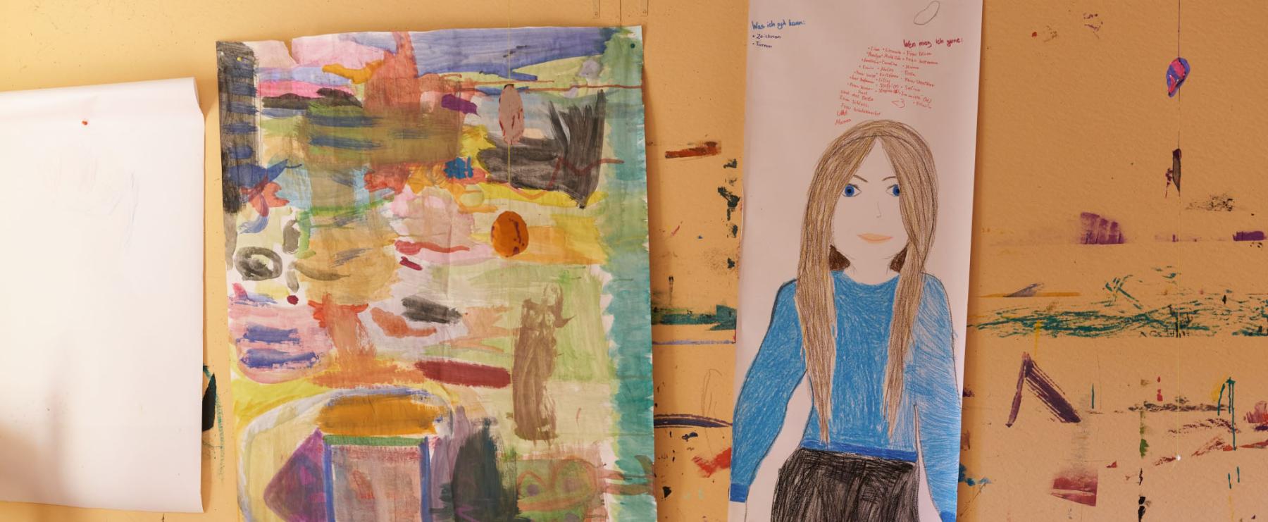 Zwei Kinderzeichnungen an einer Wand: eine bunte abstrakte Malerei und das Porträt eines Mädchens mit braunen Haaren.