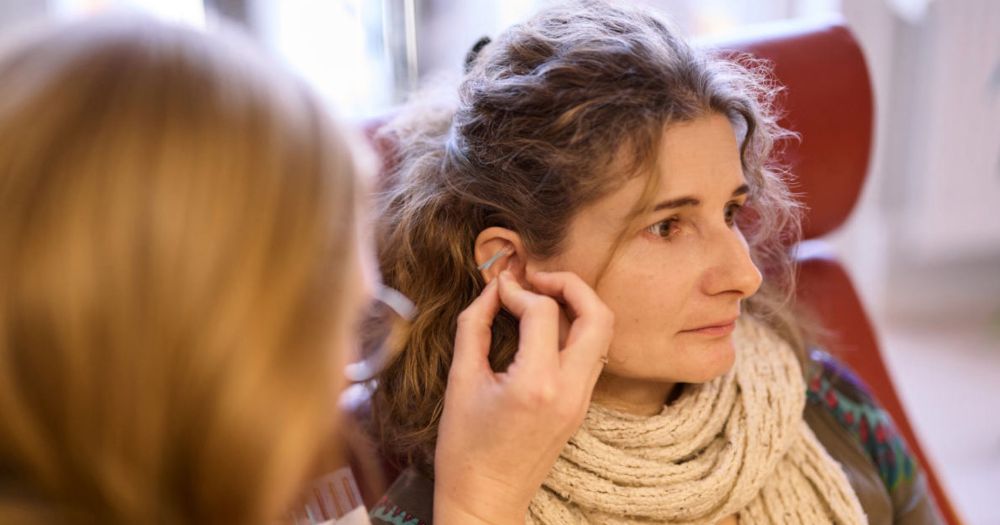 Nahaufnahme einer Frau, die eine Ohrakupunktur erh?lt. Die Therapeutin setzt vorsichtig eine kleine Nadel in ihr Ohr.