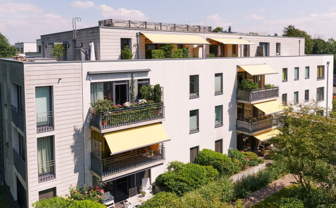 Luftaufnahme auf ein Mehrfamilienhaus mit Balkonen, Markisen und ?ppiger Begr?nung an einem sonnigen Tag.