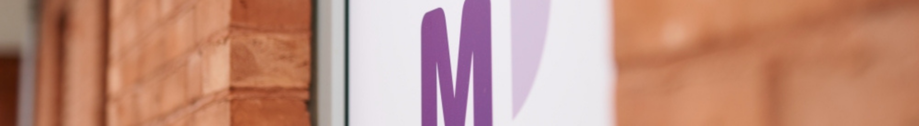 Ausschnitt eines Schildes mit dem Logo der Martha Stiftung an einer Backsteinfassade.